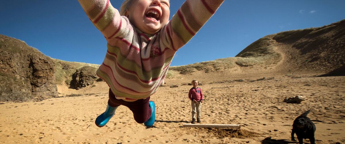 A child playing on a sandy beach with a dog and a person in the background.