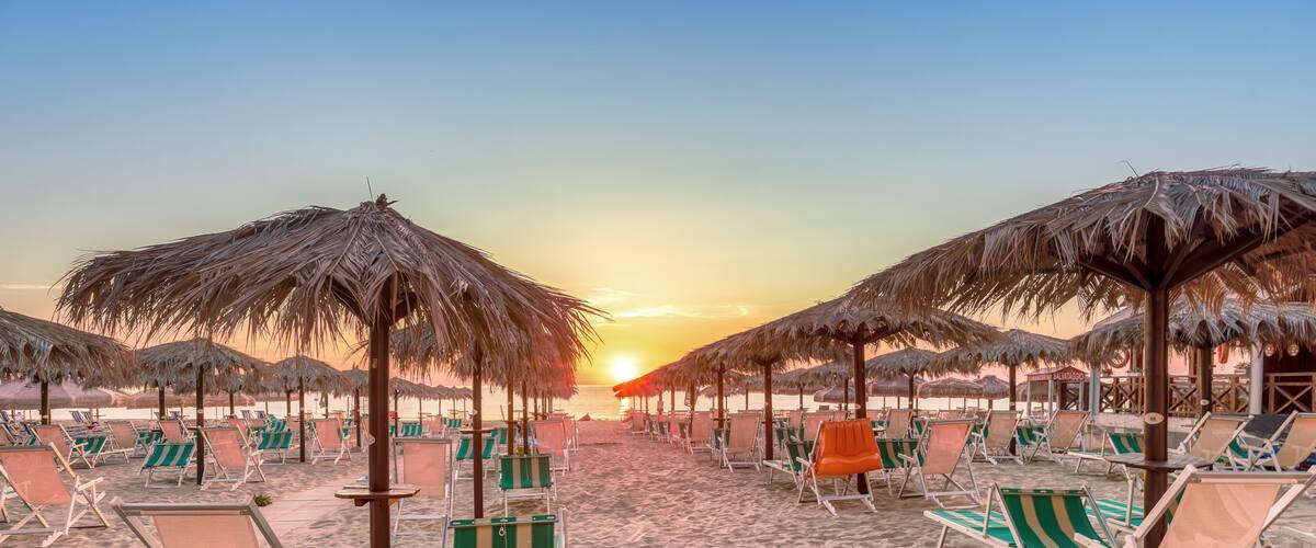 A beach with rows of beach chairs and thatched umbrellas under a sunset sky.