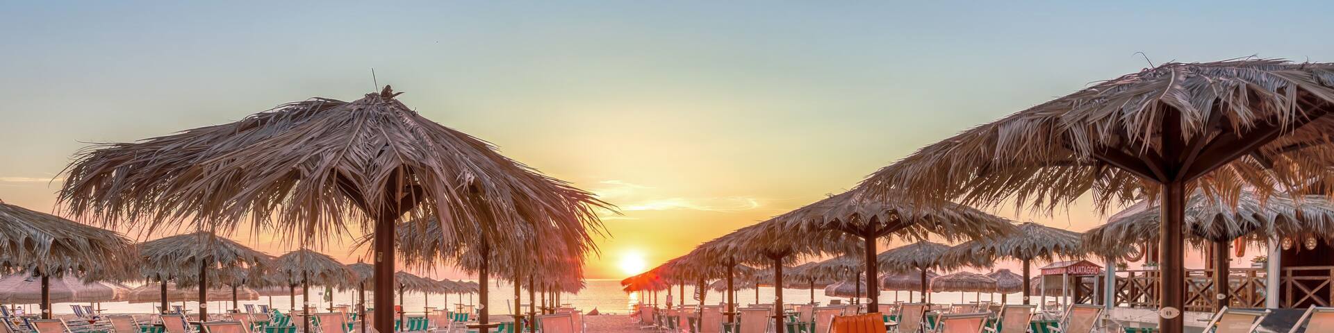 A beach with rows of beach chairs and thatched umbrellas under a sunset sky.