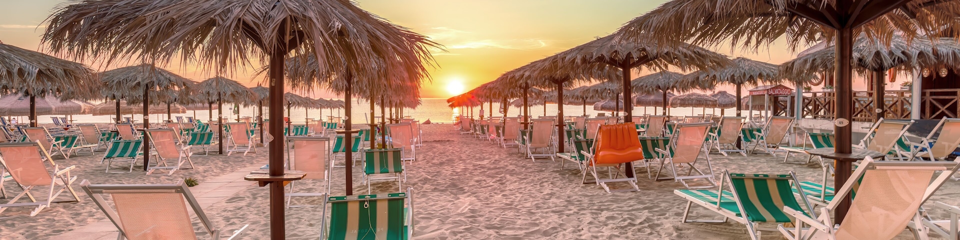 A beach with rows of beach chairs and thatched umbrellas under a sunset sky.