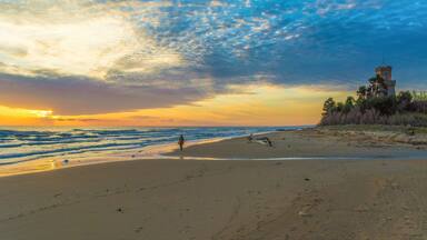 A beach with a tower and ocean waves at sunset.
