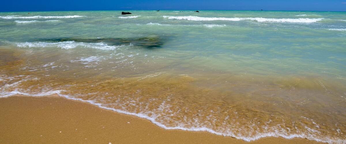 A beach with clear turquoise water, gentle waves, and a sandy shore.