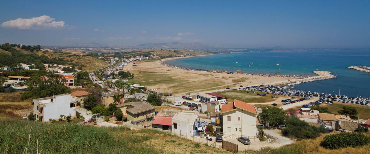 A coastal town with a beach, parked cars, and a clear blue sky.