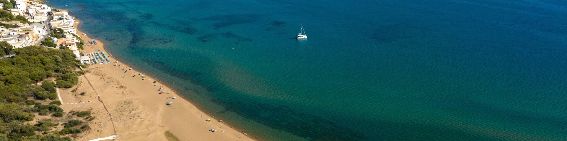An aerial view of a coastal area with a sandy beach, a small boat, and a river flowing into the sea.