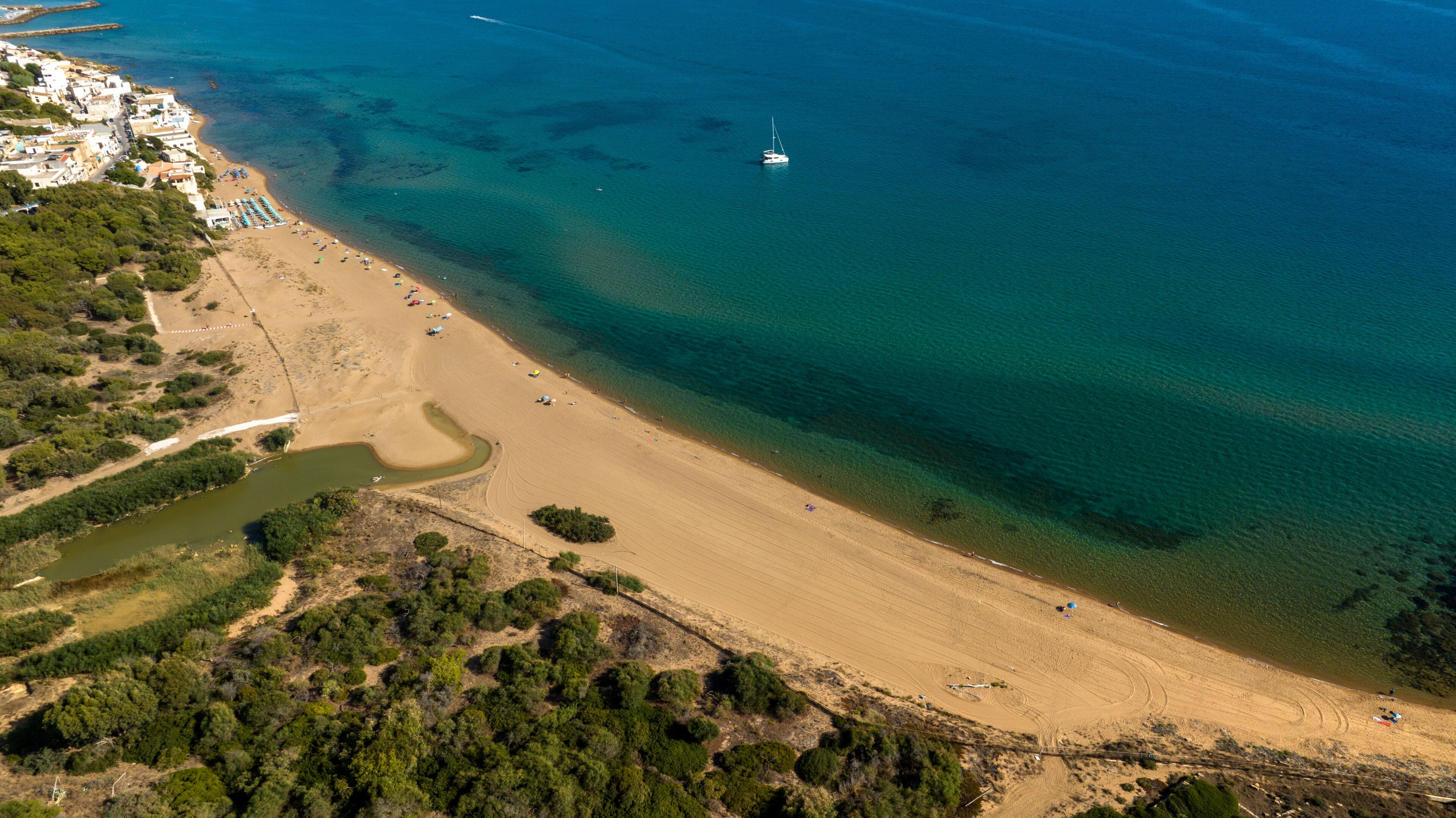 An aerial view of a coastal area with a sandy beach, a small boat, and a river flowing into the sea.