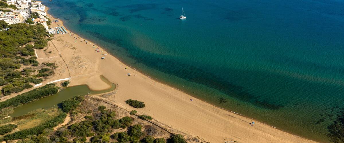 An aerial view of a coastal area with a sandy beach, a small boat, and a river flowing into the sea.