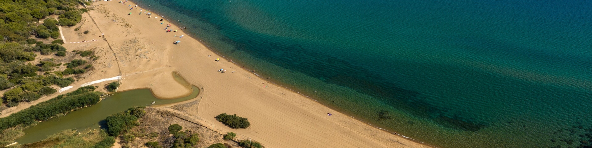 An aerial view of a coastal area with a sandy beach, a small boat, and a river flowing into the sea.