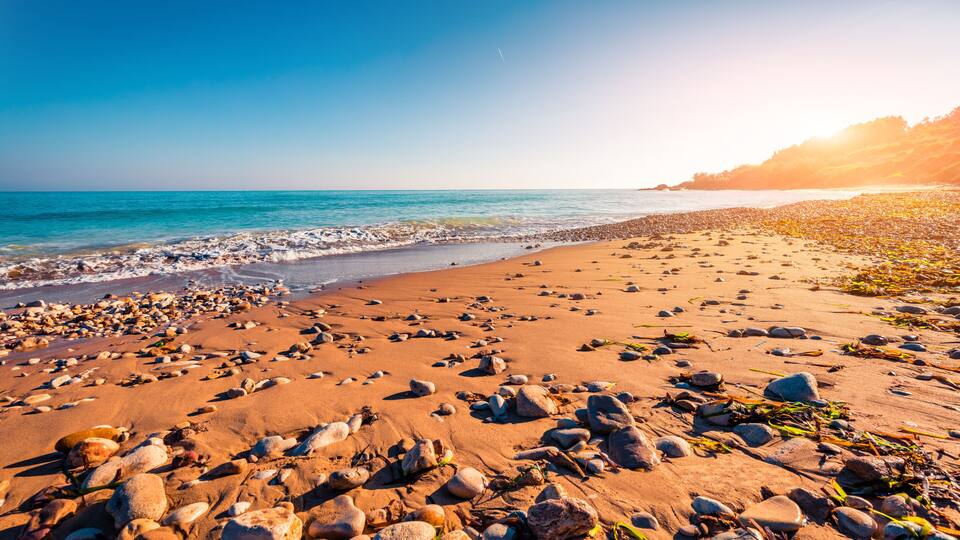 A rocky beach with clear blue water and a sunset.