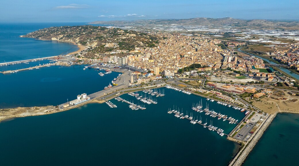 An aerial view of a coastal city with a marina filled with boats, a large urban area, and a hilly landscape in the background.