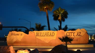 Um grande letreiro iluminado de boas-vindas para Bullhead City, Arizona, com palmeiras e rochas ao redor.