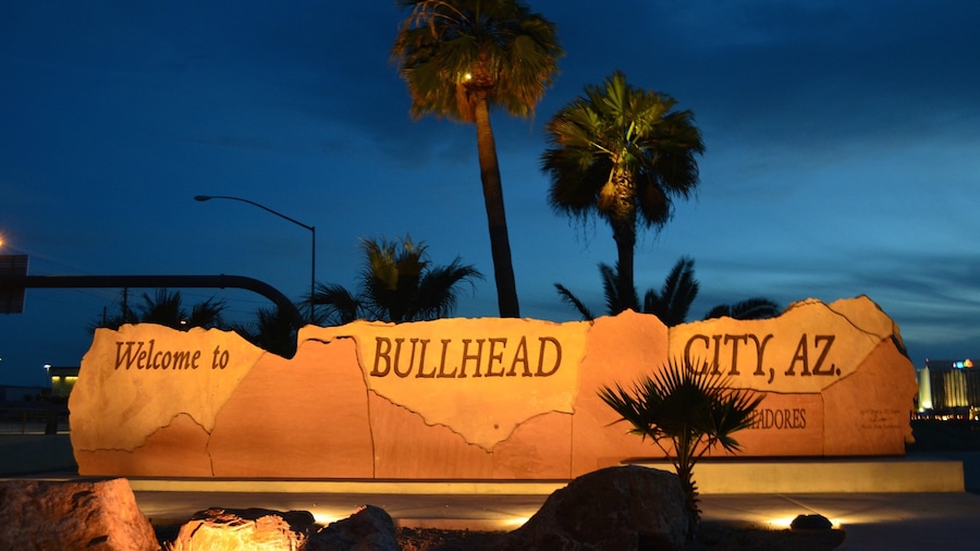 Um grande letreiro iluminado de boas-vindas para Bullhead City, Arizona, com palmeiras e rochas ao redor.