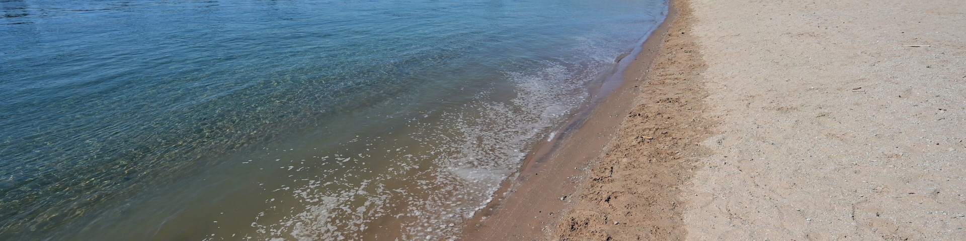 Orilla de río con aguas cristalinas, una playa arenosa y montañas a lo lejos.