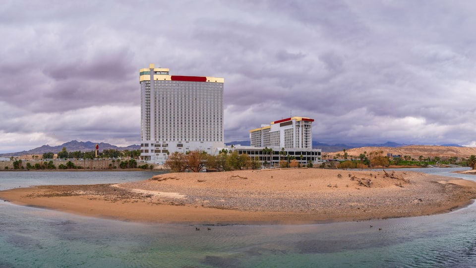 A river with a sandy island, a tall building, and mountains in the background.