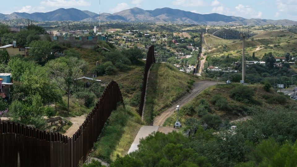 A rural landscape with a wooden fence, a dirt path, and distant mountains.