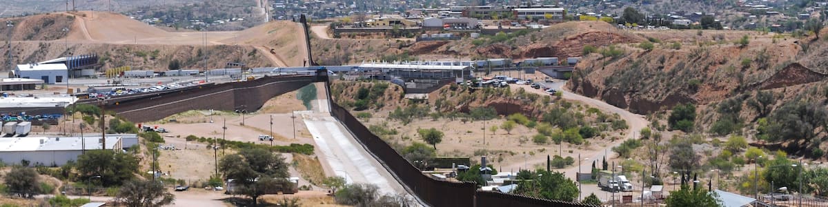 A dam with a spillway, a highway, and a town in a hilly desert landscape.