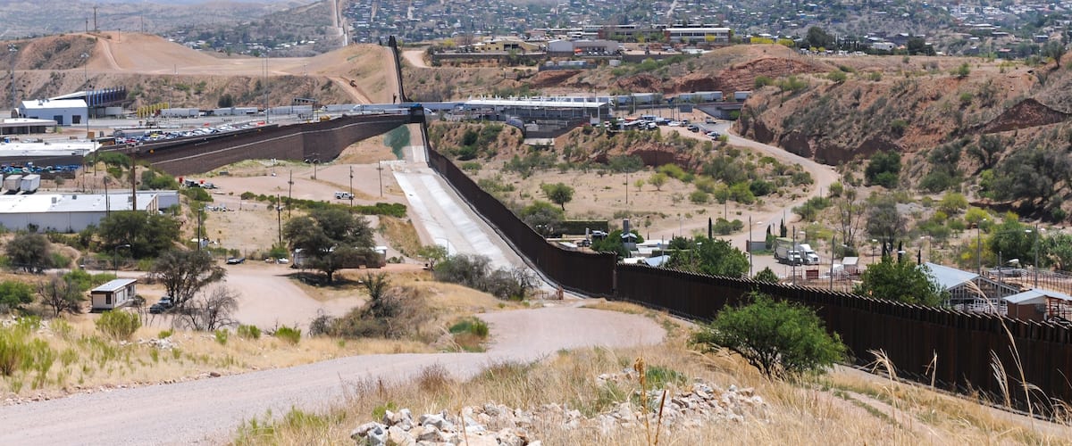 A dam with a spillway, a highway, and a town in a hilly desert landscape.