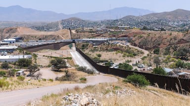 Uma barragem com vertedouro, uma autoestrada e uma cidade em uma paisagem desértica e montanhosa.