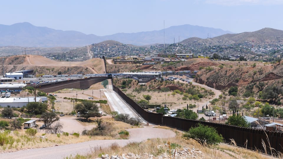 A dam with a spillway, a highway, and a town in a hilly desert landscape.