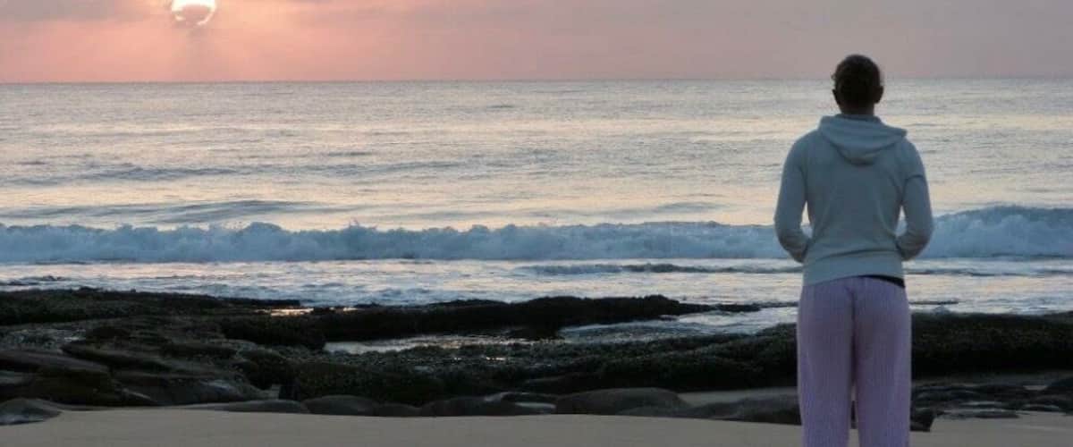 A person standing on a beach facing the ocean at sunset.