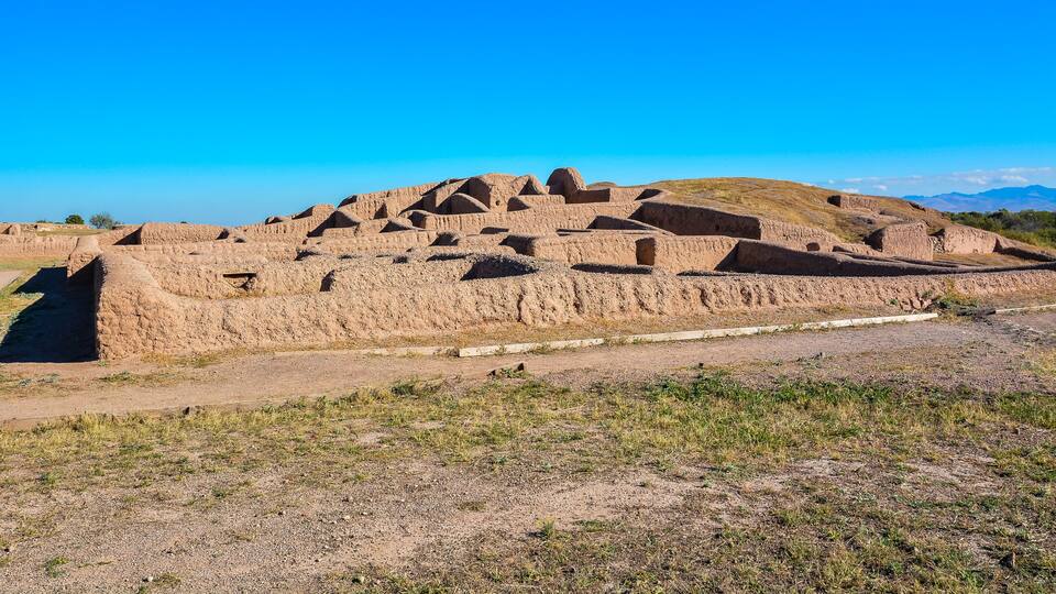 Ancient terraced structures in a dry, grassy landscape with mountains in the background.