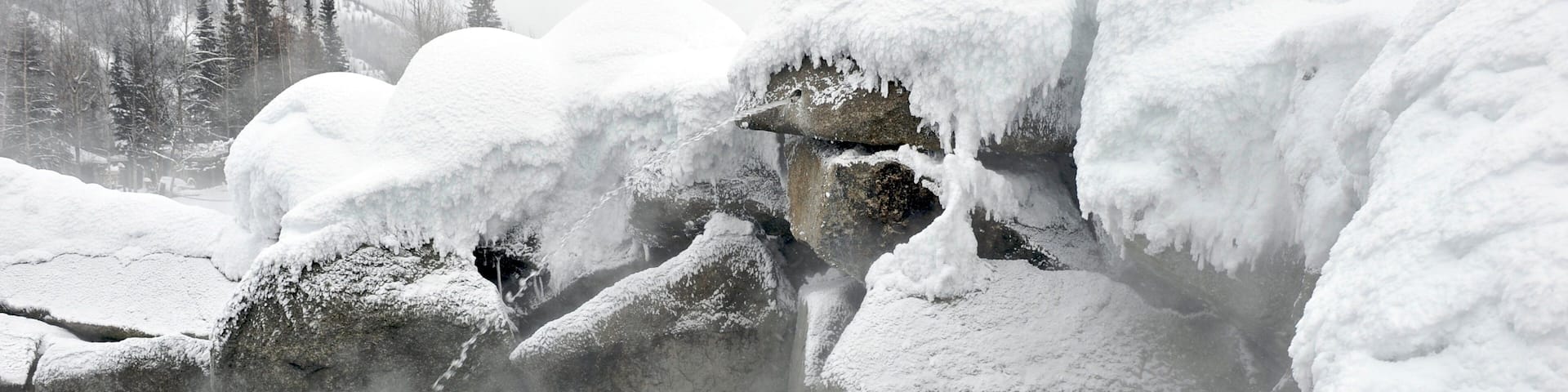 A couple in a hot spring surrounded by snow-covered rocks.