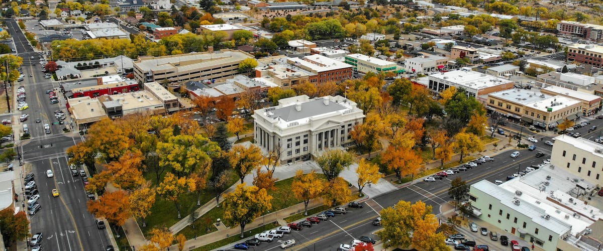 A cityscape with autumn foliage, a prominent white building, and mountains in the background.
