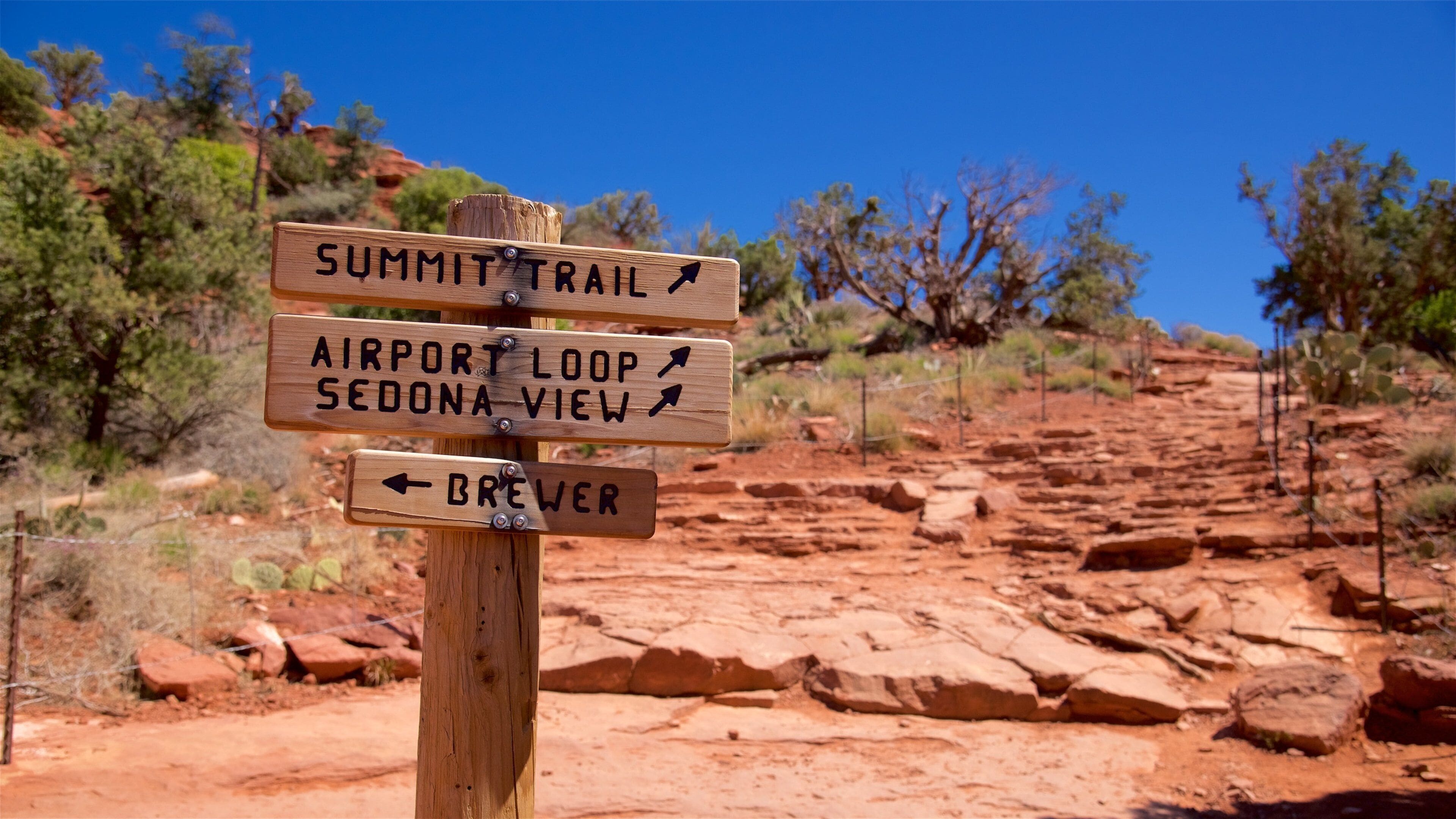 Een houten bord met aanduidingen naar Summit Trail, Airport Loop, Sedona View en Brewer.