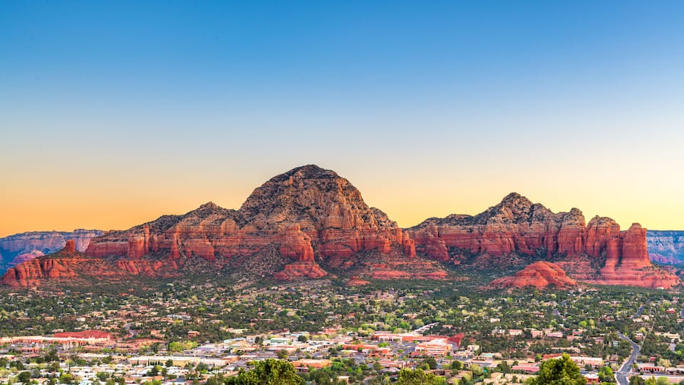 A town nestled at the base of a prominent red rock mountain range with a clear sky.