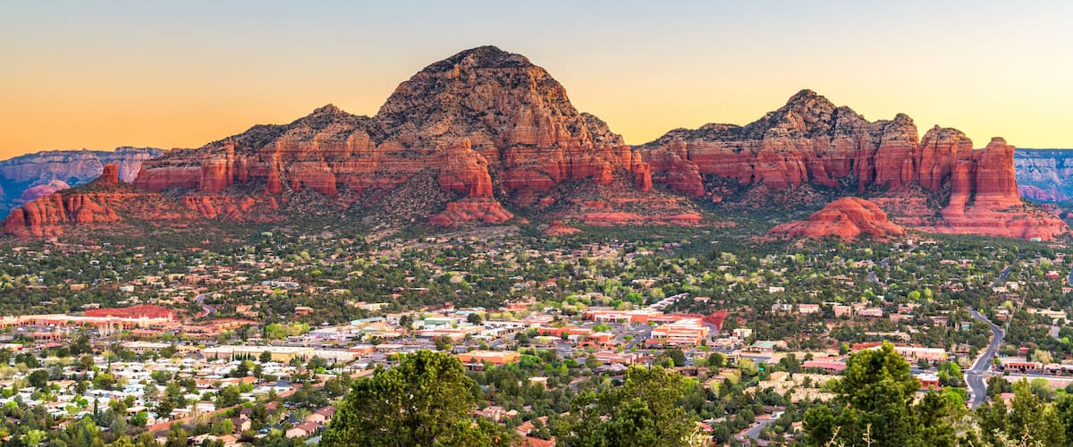 A town nestled at the base of a prominent red rock mountain range with a clear sky.