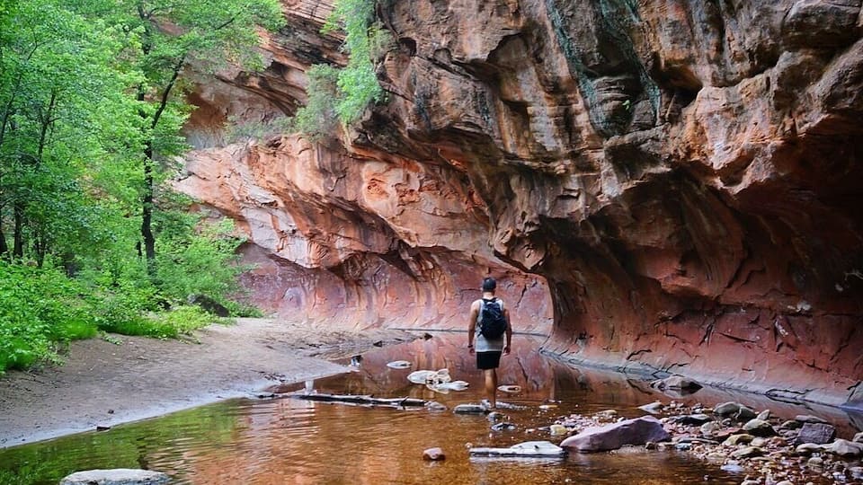 A hiker walking through a rocky canyon with a river.