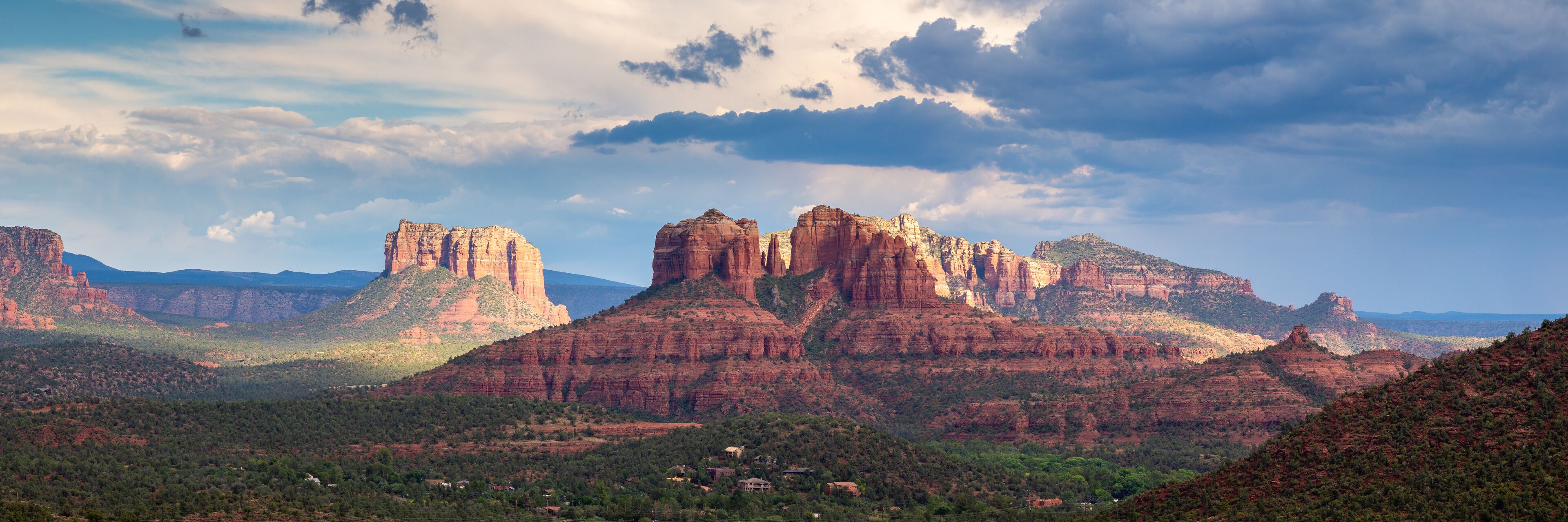 A canyon landscape with prominent red rock formations and scattered houses.
