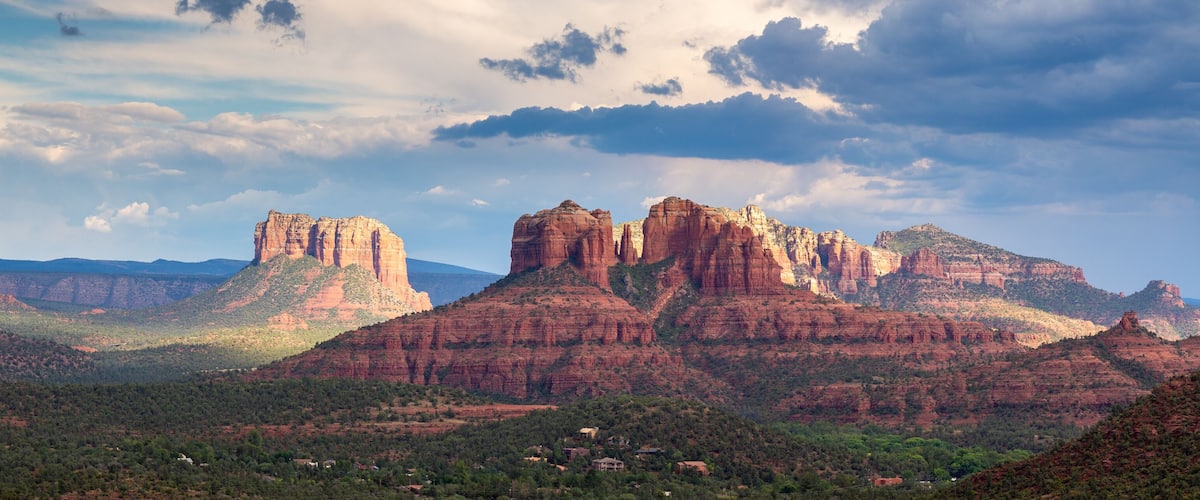 A canyon landscape with prominent red rock formations and scattered houses.