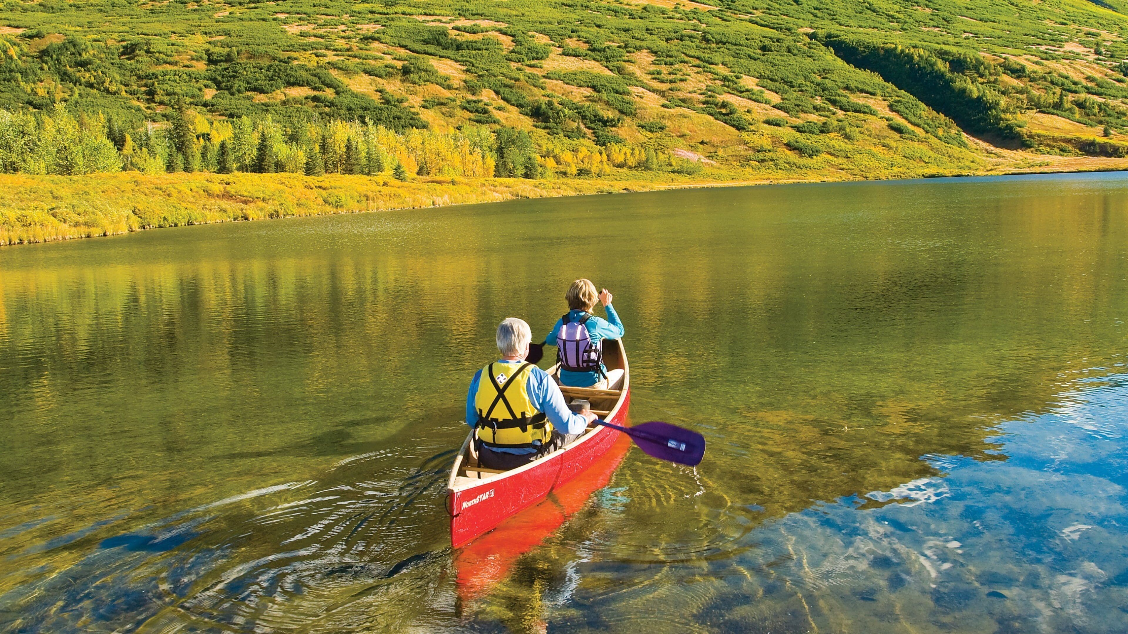 A red canoe on a calm lake surrounded by green hills.