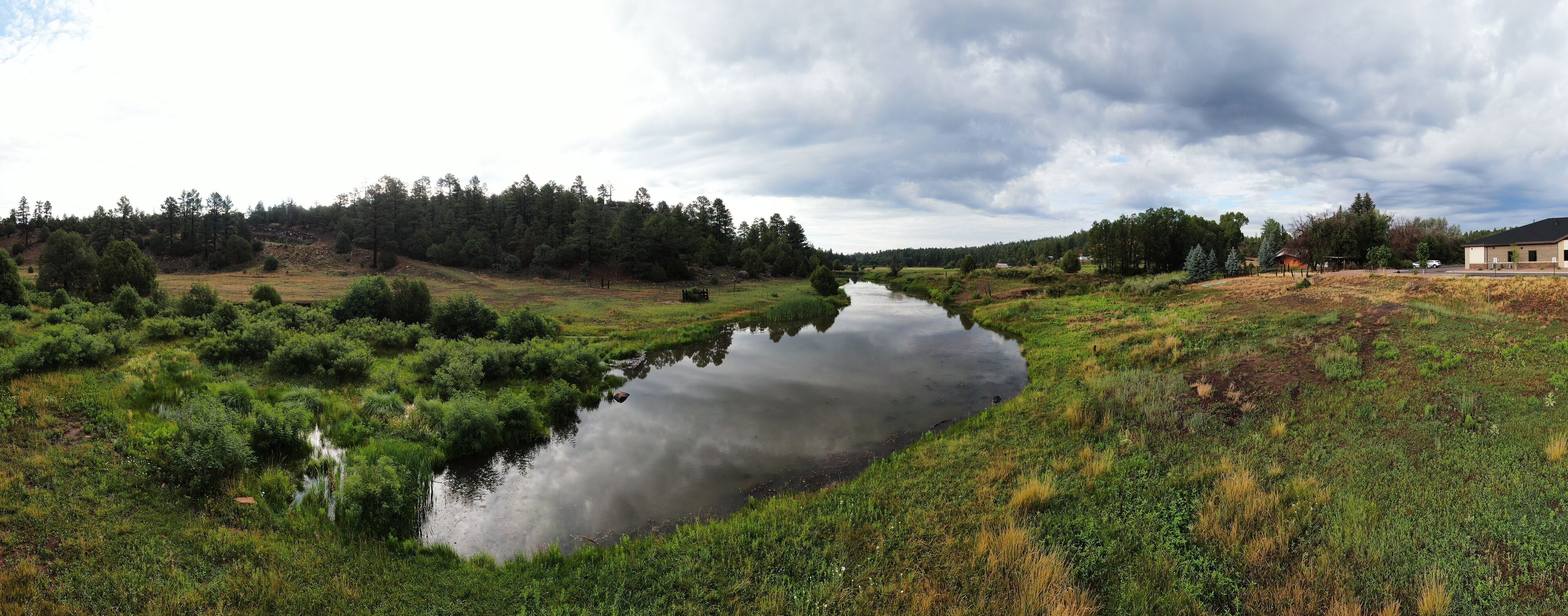 A river winding through a grassy landscape with trees and a building in the distance.