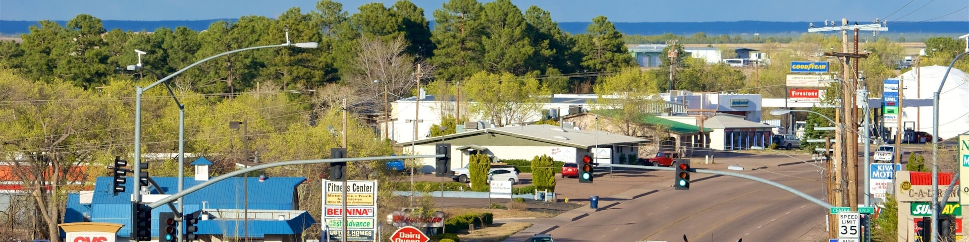 A busy intersection with multiple lanes of traffic, including cars and trucks. Visible businesses include CVS Pharmacy, a fitness center, and a Kiva Motti's. There are traffic lights and street signs indicating a speed limit of 35 mph.