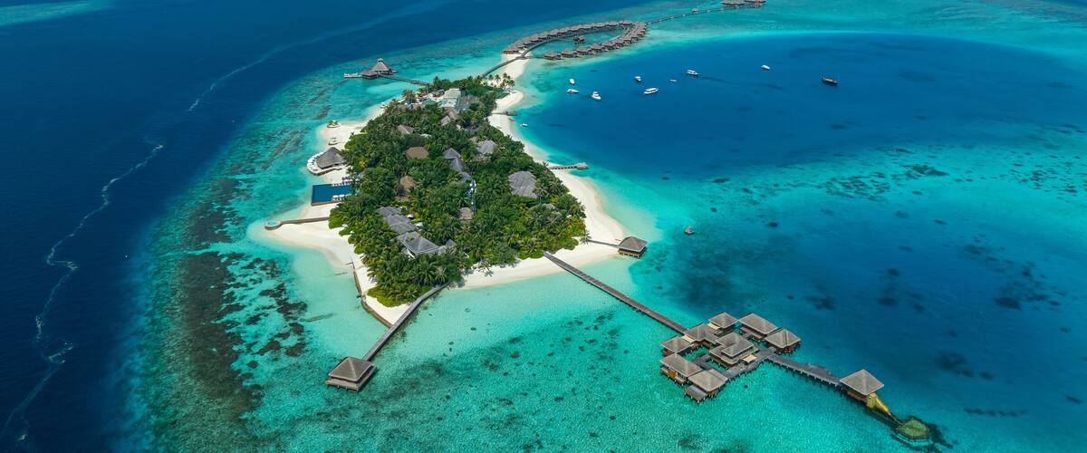 Aerial view of bungalows of a luxury hotel on Huvafen Fushi island at sunset on Maldives archipelagos.