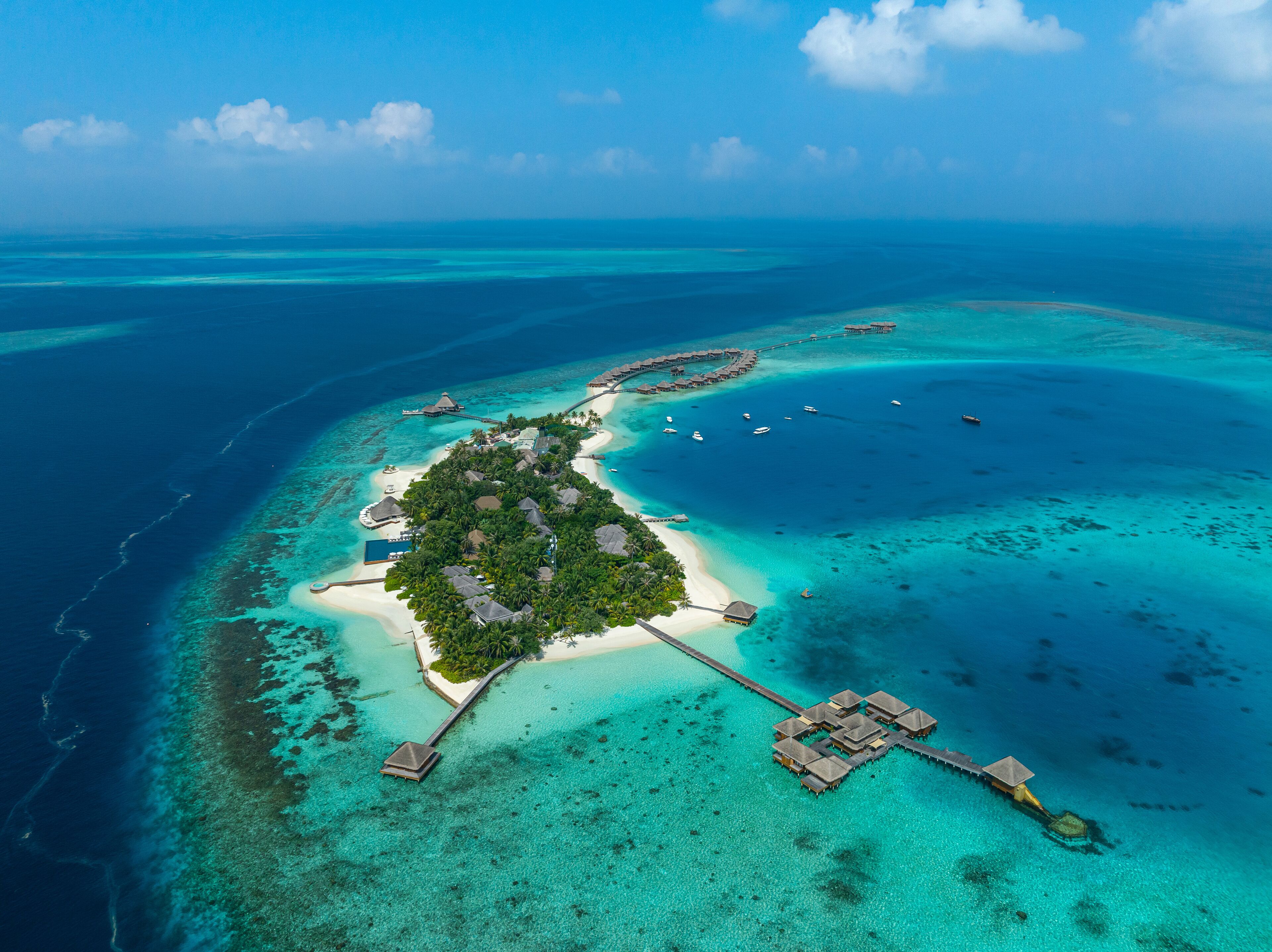 An aerial view of a tropical island with clear turquoise waters, white sandy beaches, and overwater bungalows.