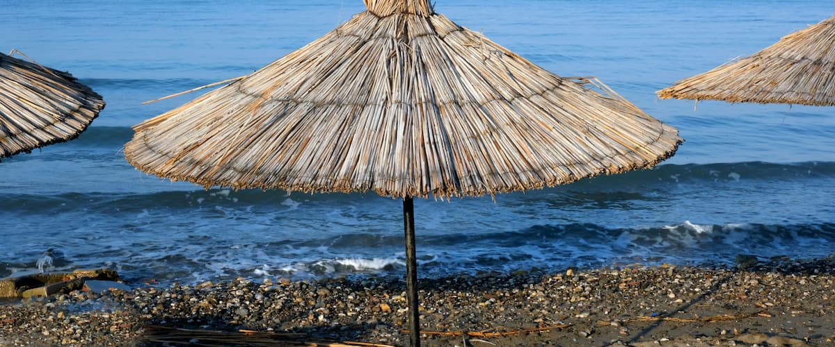 A beach with thatched umbrellas and pebbled shoreline.