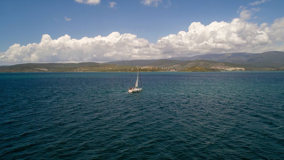 A sailboat on a calm sea with a mountainous coastline in the background.