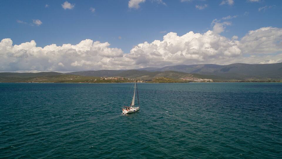 A sailboat on a calm sea with mountains in the background.