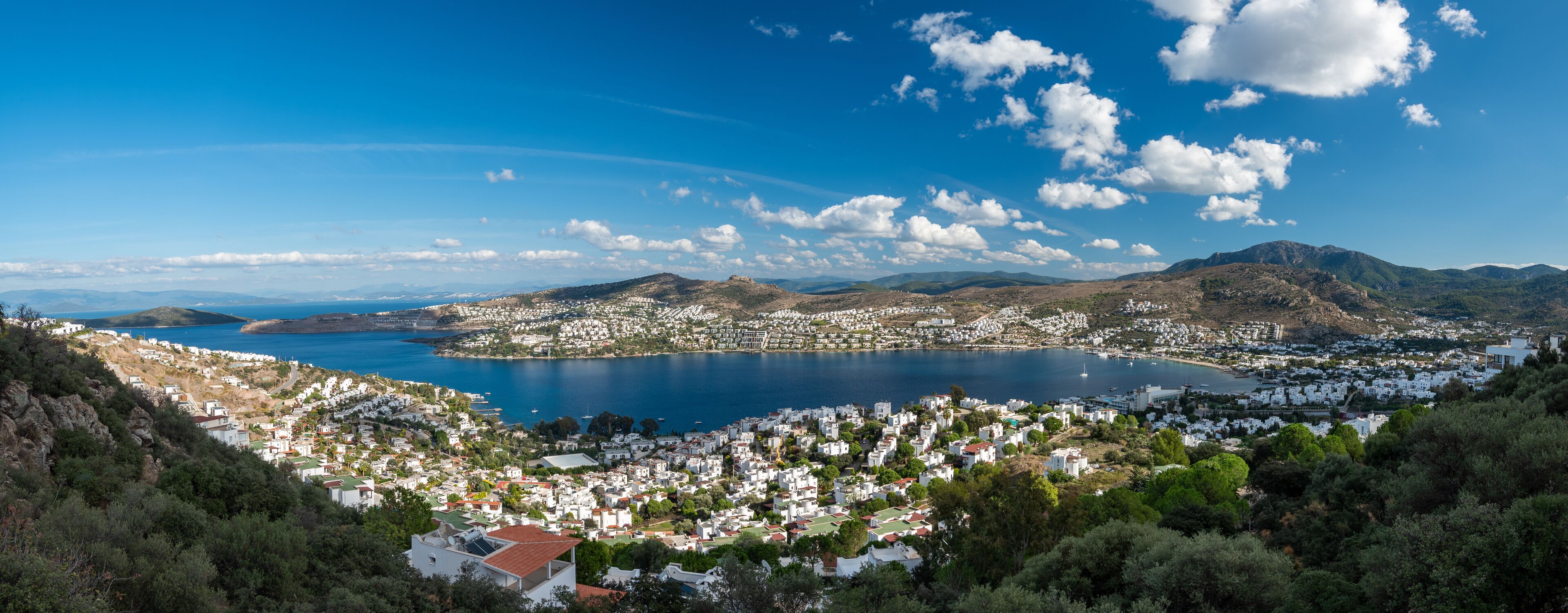 A coastal town with white buildings, a large bay, and mountains in the background.