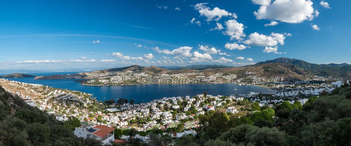 A coastal town with white buildings, a large bay, and mountains in the background.