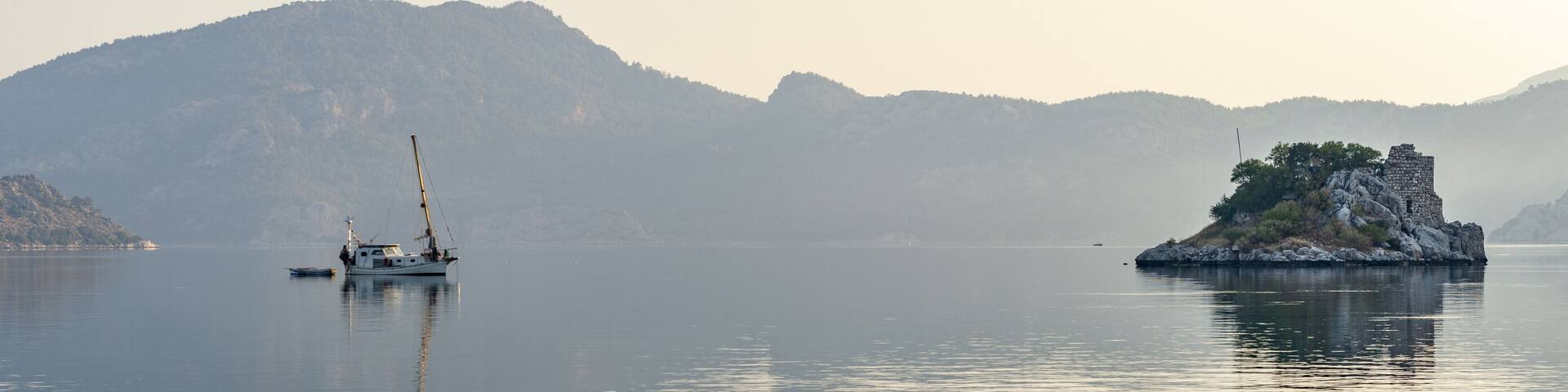A calm lake with a small boat and a rocky island with ruins.