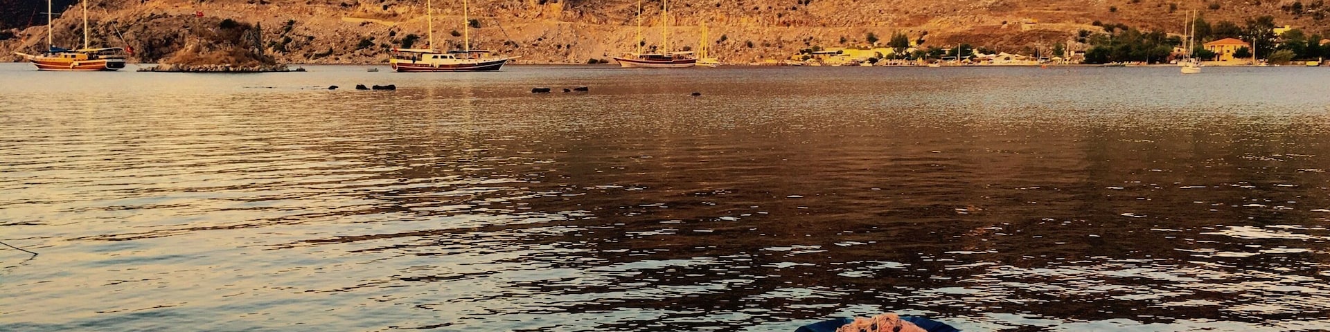 A calm lake with a small boat tied to a dock, surrounded by rocky hills and sparse vegetation.