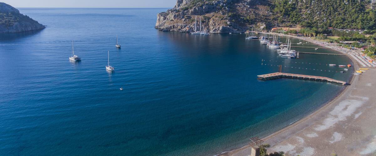 A coastal bay with clear blue waters, boats, a rocky shoreline, and a small pier.