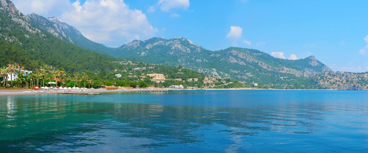 A coastal town with a beach, mountains, and clear blue water.