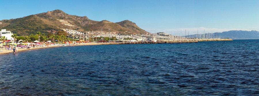 Un pueblo costero con playa, montañas y puerto con barcos.