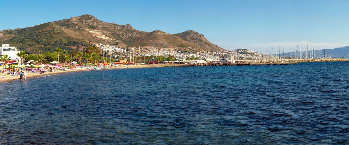 A coastal town with a beach, mountains, and a harbor with boats.