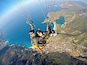 Deux personnes pratiquent le parapente au-dessus d’un paysage côtier, avec une ville en contrebas.