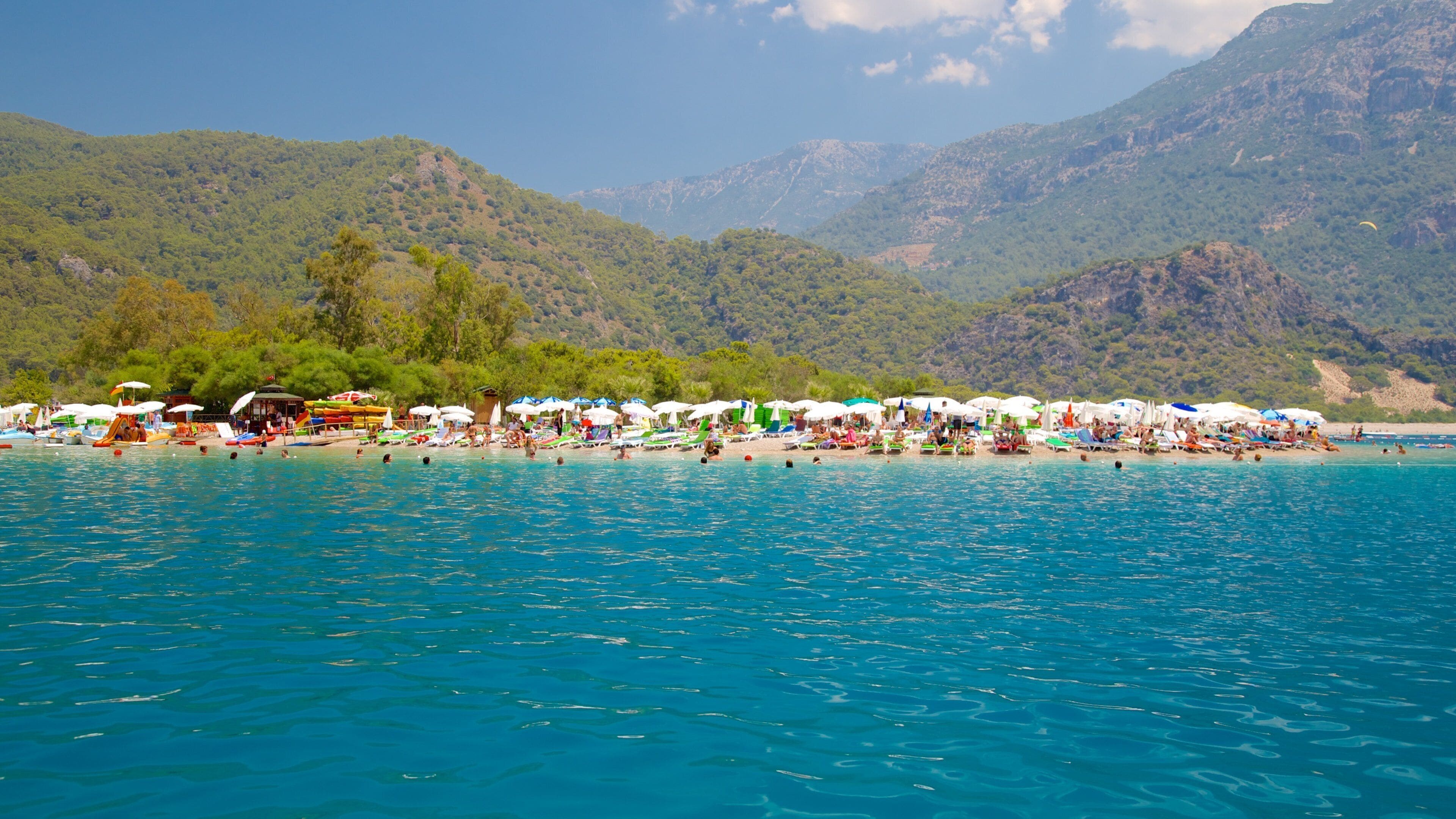 A beach with clear blue water, umbrellas, and people.